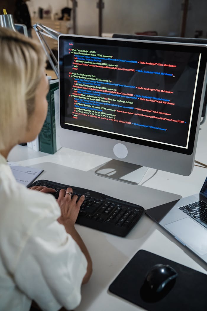 services-04 A female programmer writing code on a desktop computer in an office setting with a focus on technology and IT development.